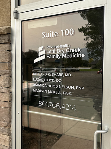 Vinyl lettering on outside entry door, showing medical providers, Revere Health company logo and office phone contact number.