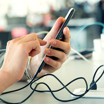 Photograph showing close up of hand holding a phone while phone is charging.