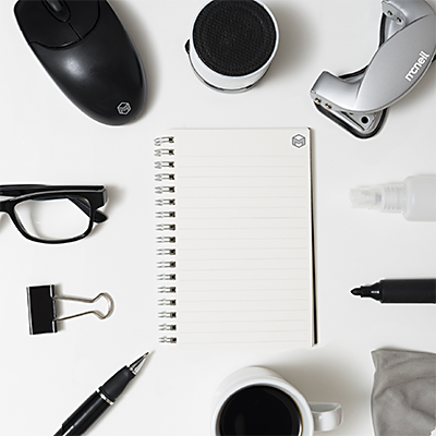 Photograph showing downward view of office supplies: mouse, stapler, a pair of reading glasses, a large clip, a pen, a cup of coffee, a micro fiber cloth, a desk speaker, a marker and a small spray bottle.