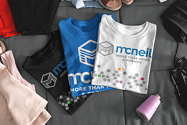Image showing three T-Shirts, black, blue and white, overlaid and showing the McNeil Prining and Promos logo.