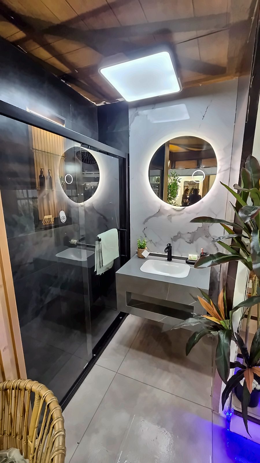 Bathroom set inside the JOONG booth with a lit round mirror, marble-look wall and shower enclosure